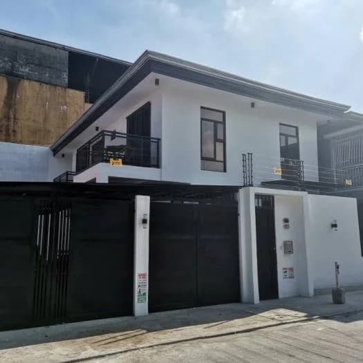 Completed two-storey house with white walls, dark window frames, and a black steel gate